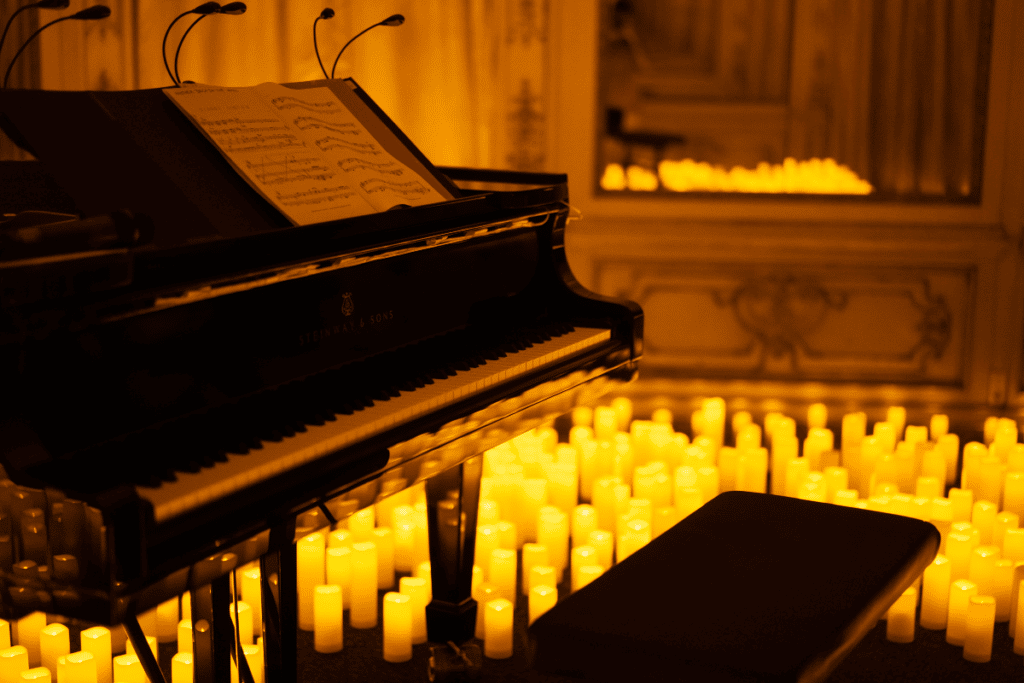 Un concert Candlelight avec un piano à queue noir avec une partition et des dizaines de bougies dans le fond et sur le sol. 