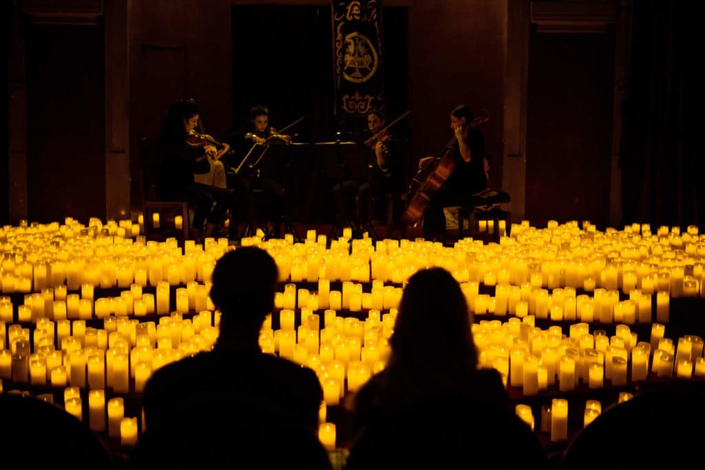 Photo du public à contre jour regardant et écoutant un concert Candlelight interprété par un quatuor à cordes