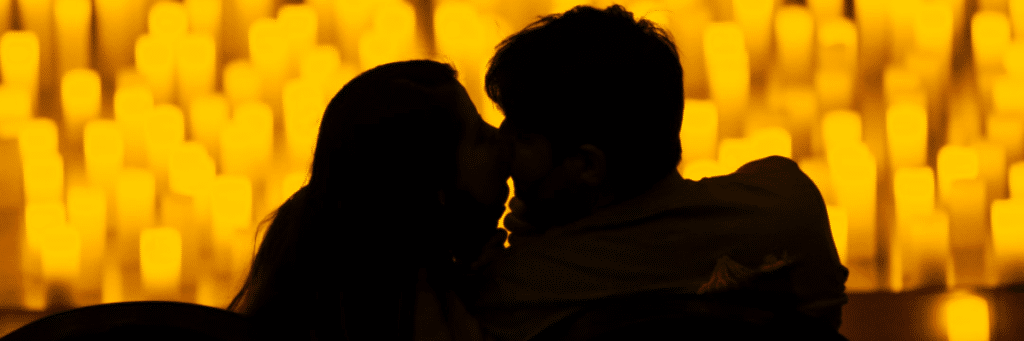 Photo d'un couple qui s'embrasse à contre jour devant les milliers de bougies d'un concert Candlelight